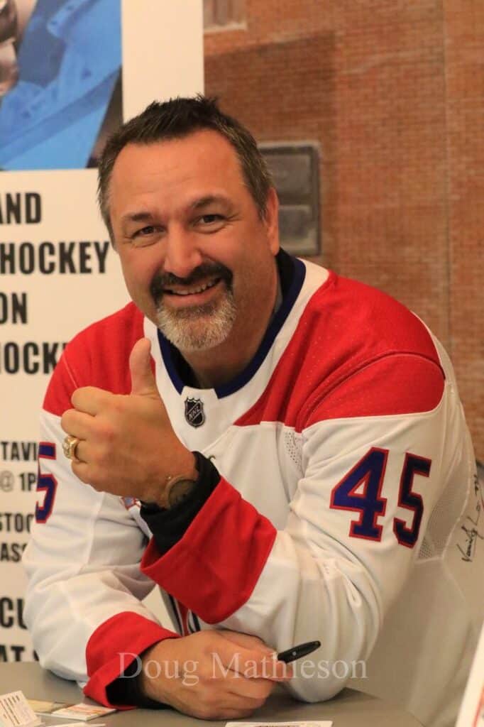 Man in hockey jersey at Contest MIB event, smiling and giving thumbs up.